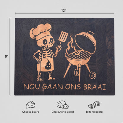 A premium everyday end-grain cutting board with Brass feet.

Materials: Base is walnut wood with a hard maple inlay.

Design: With a carved skeleton chef grilling next to a charcoal grill, with the text 'NOU GAAN ONS BRAAI' below.

Uses:
- Chopping Board
- Cheese or Meat Board
- Charcuterie Board
- Biltong Board

Note: Wood is a natural material, and the received product will have wood color and grain variations compared to this picture.