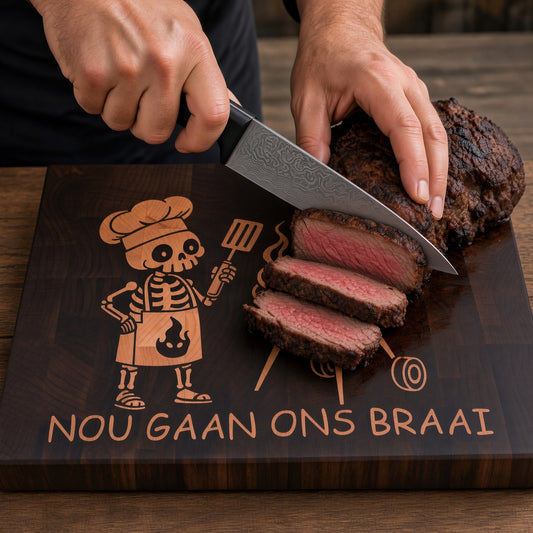 A premium everyday end-grain cutting board with Brass feet.

Materials: Base is walnut wood with a hard maple inlay.

Design: With a carved skeleton chef grilling next to a charcoal grill, with the text 'NOU GAAN ONS BRAAI' below.

Uses:
- Chopping Board
- Cheese or Meat Board
- Charcuterie Board
- Biltong Board

Note: Wood is a natural material, and the received product will have wood color and grain variations compared to this picture.